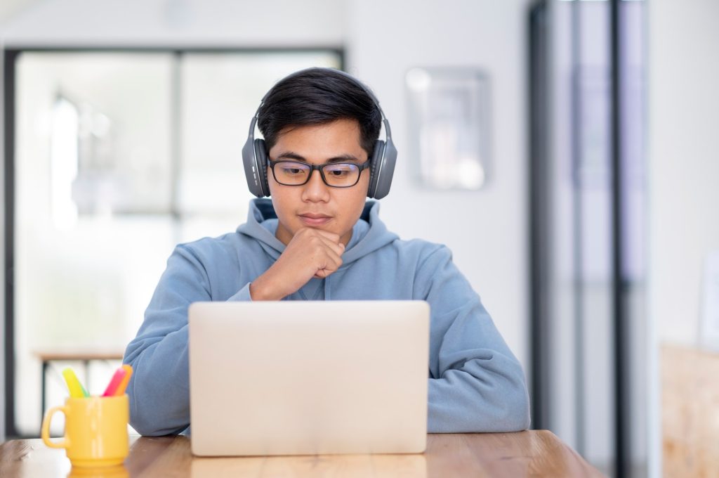 young-asian-student-man-wearing-headset-and-looking-at-laptop-display-for-learning-online-course
