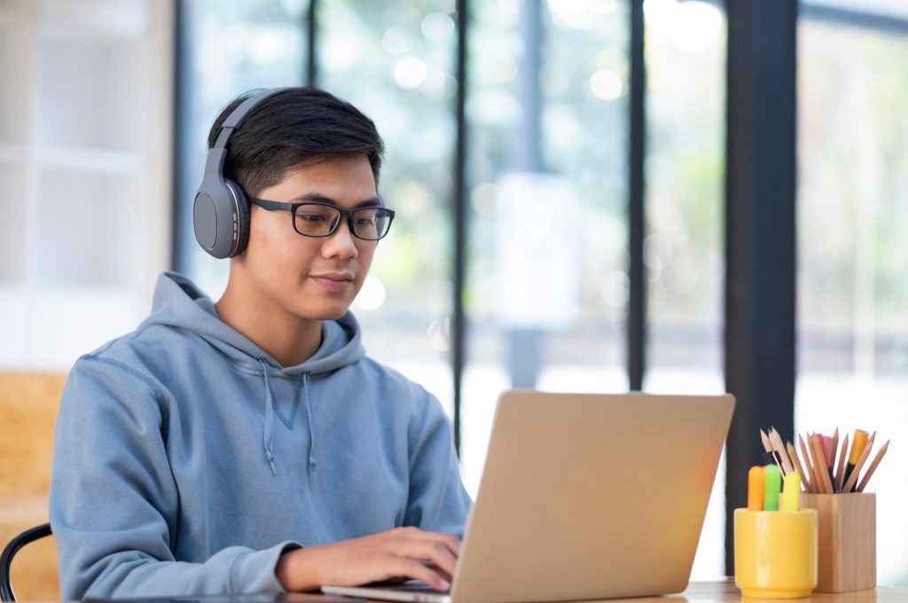 young-asian-student-man-wearing-headset-and-looking-laptop-display-for-learning-online-course-from